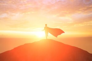 Superhero in cape running toward sunset