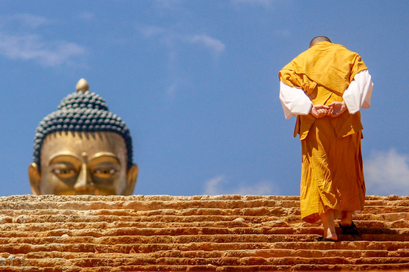 Buddhist monk climbing stairs toward statue of the Buddha