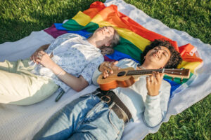 Two women relaxing on an LGBTQ+ pride flag blanket