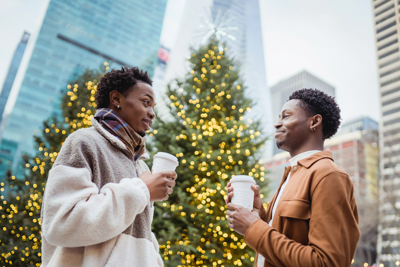 Two women holding coffee cups by a Christmas tree outside