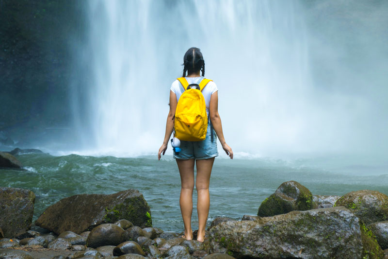Woman hiker with yellow backpack in front of waterfall