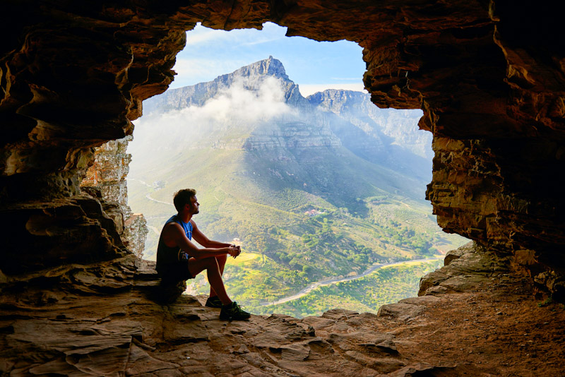 Man sitting in a cave overlooking a valley