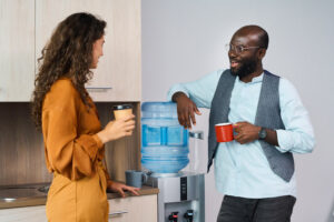 Woman and man with coffee standing by the water cooler at work